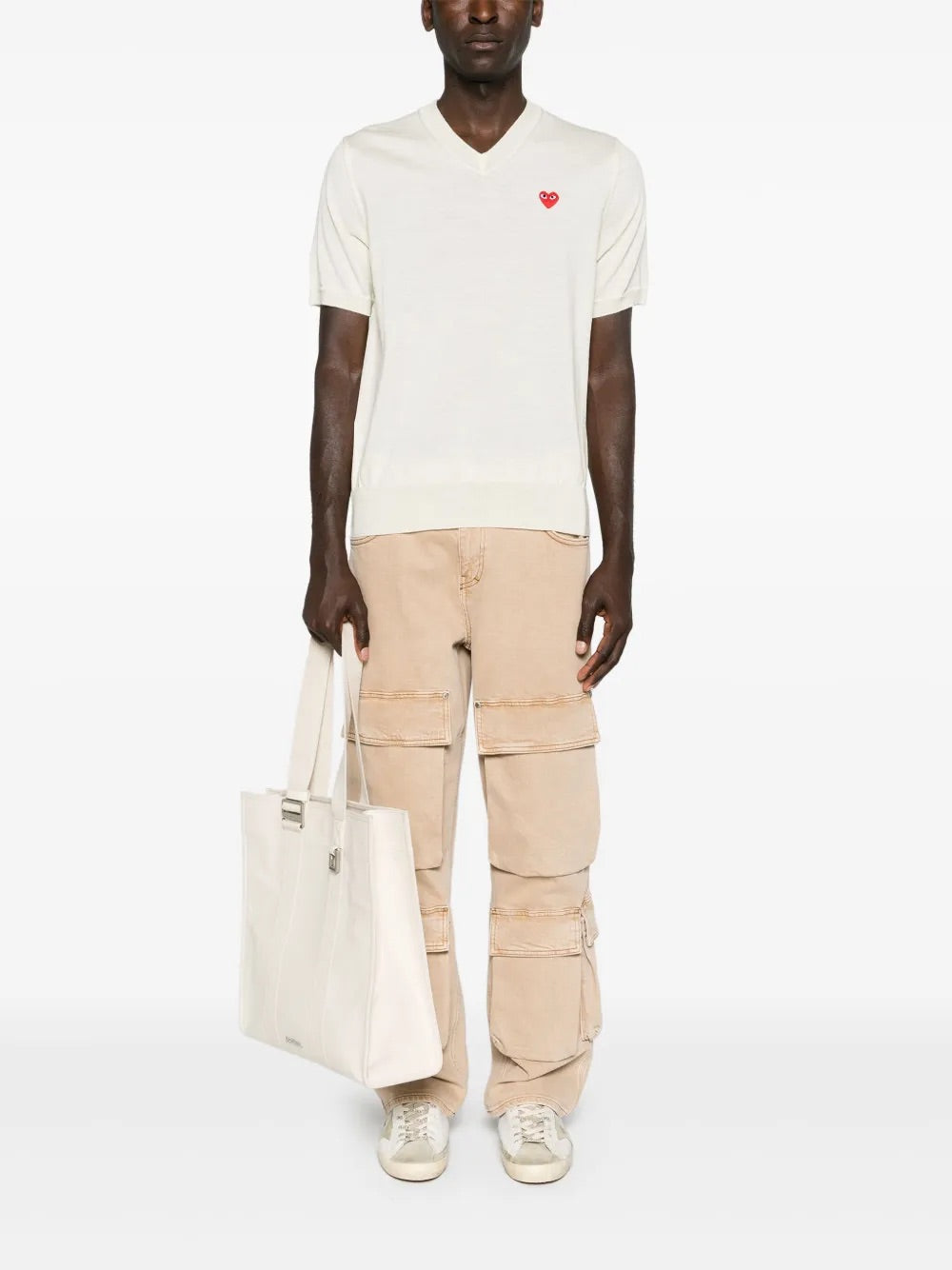 Full-body front view of a male model styled in the Comme des Garçons Play Unisex V-Neck Sweater Short-Sleeve in off white, showcasing the versatile unisex fit and minimalist wool knit design.