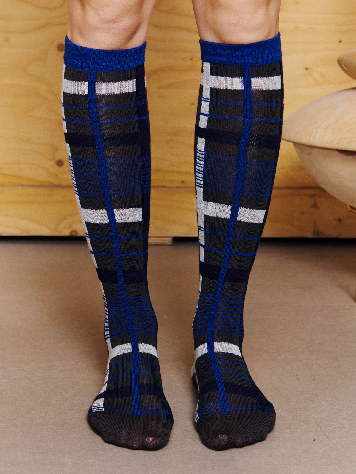 Henrik Vibskov Archive Socks in Black Blue Archive worn from the front, showing the knee-high fit, blue cuff and all-over check pattern. ID: ARCHIVE-S908