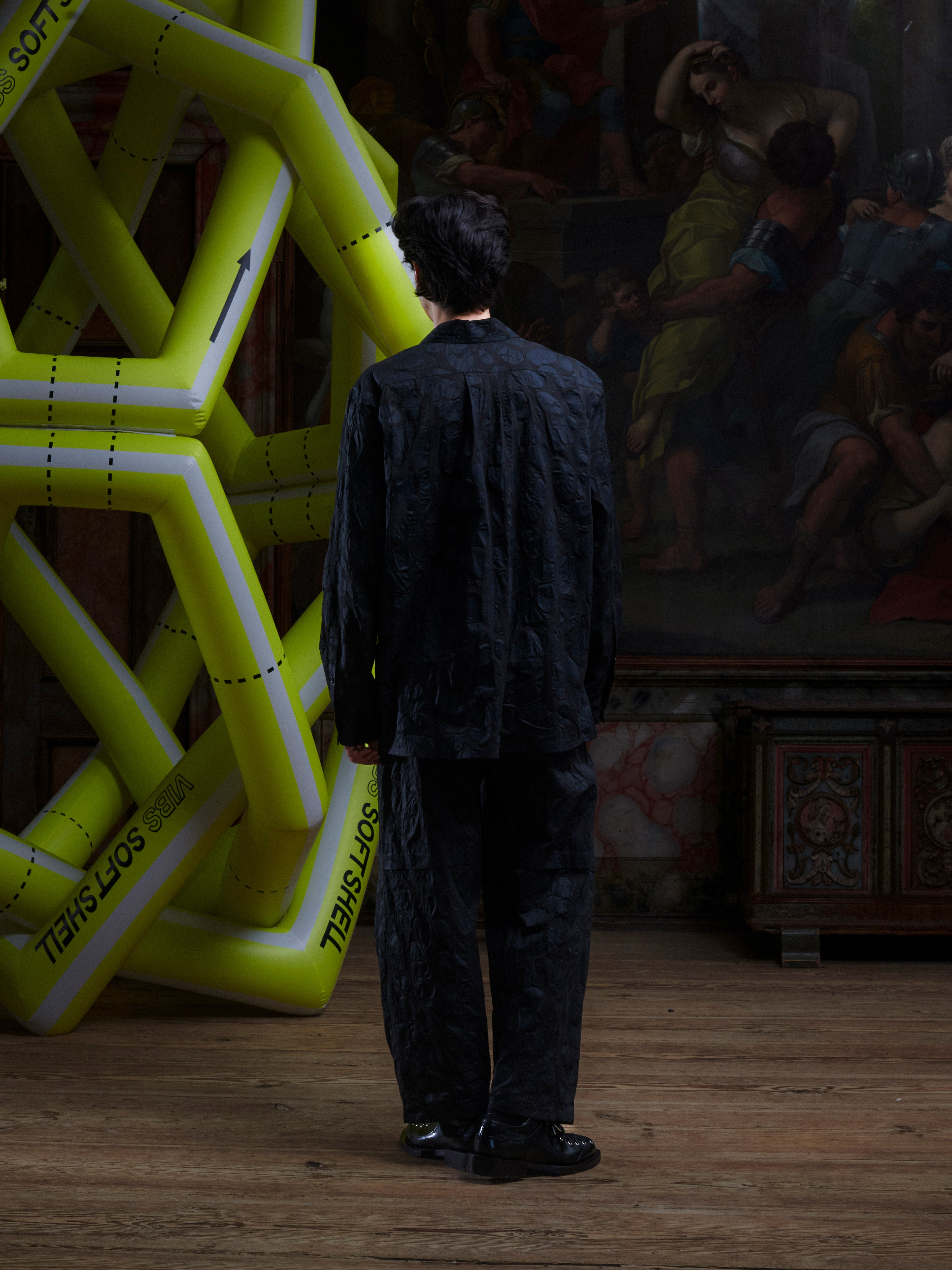Back view of male model wearing the Drawstring Pants in Black Amulets, showing the all-over black amulets pattern and relaxed straight fit.