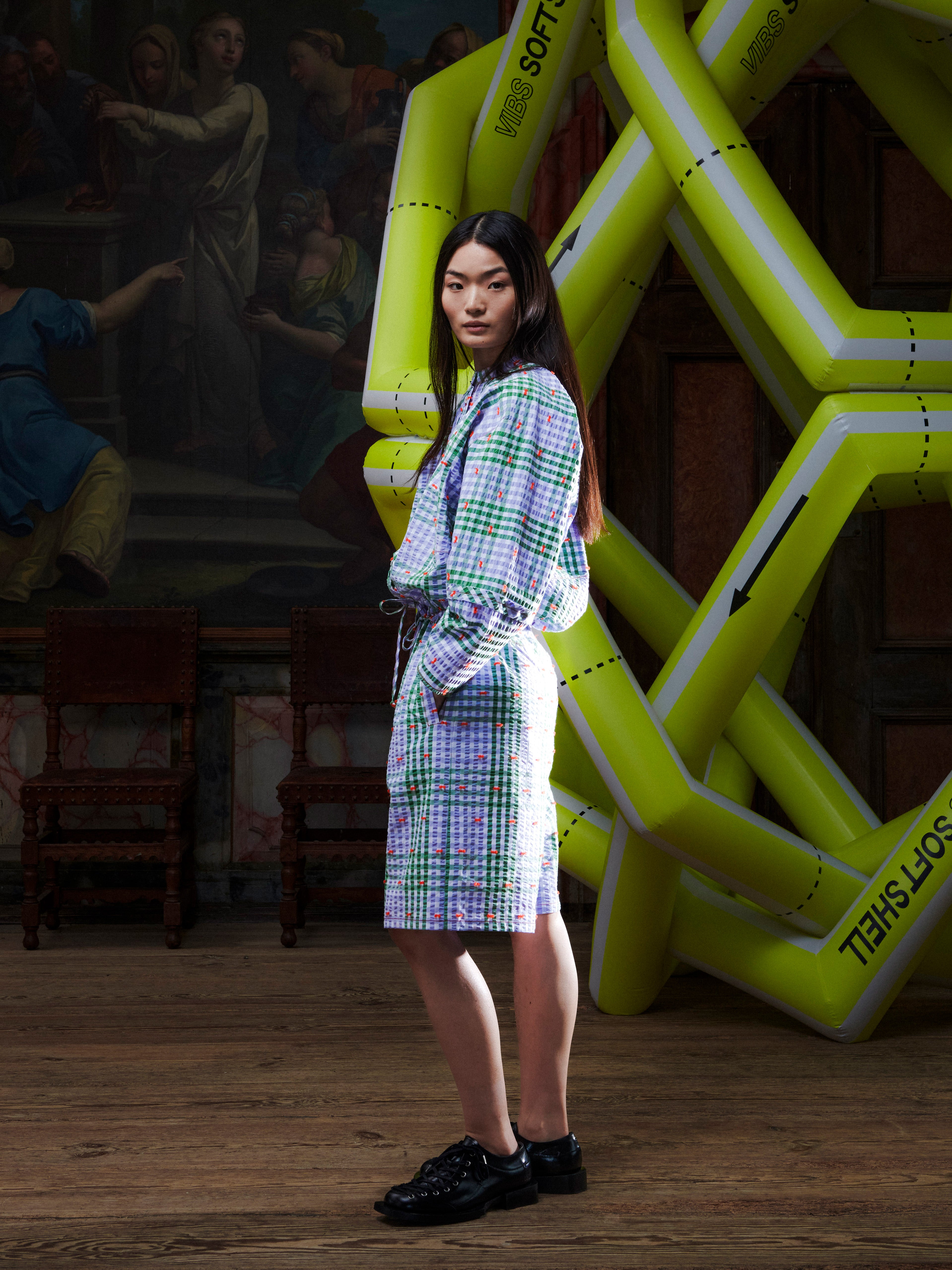 Female model wearing the Drawstring Shorts in Checks Fillé, side view, highlighting the wide leg opening, knee-length fit, and orange contrast stitching.
