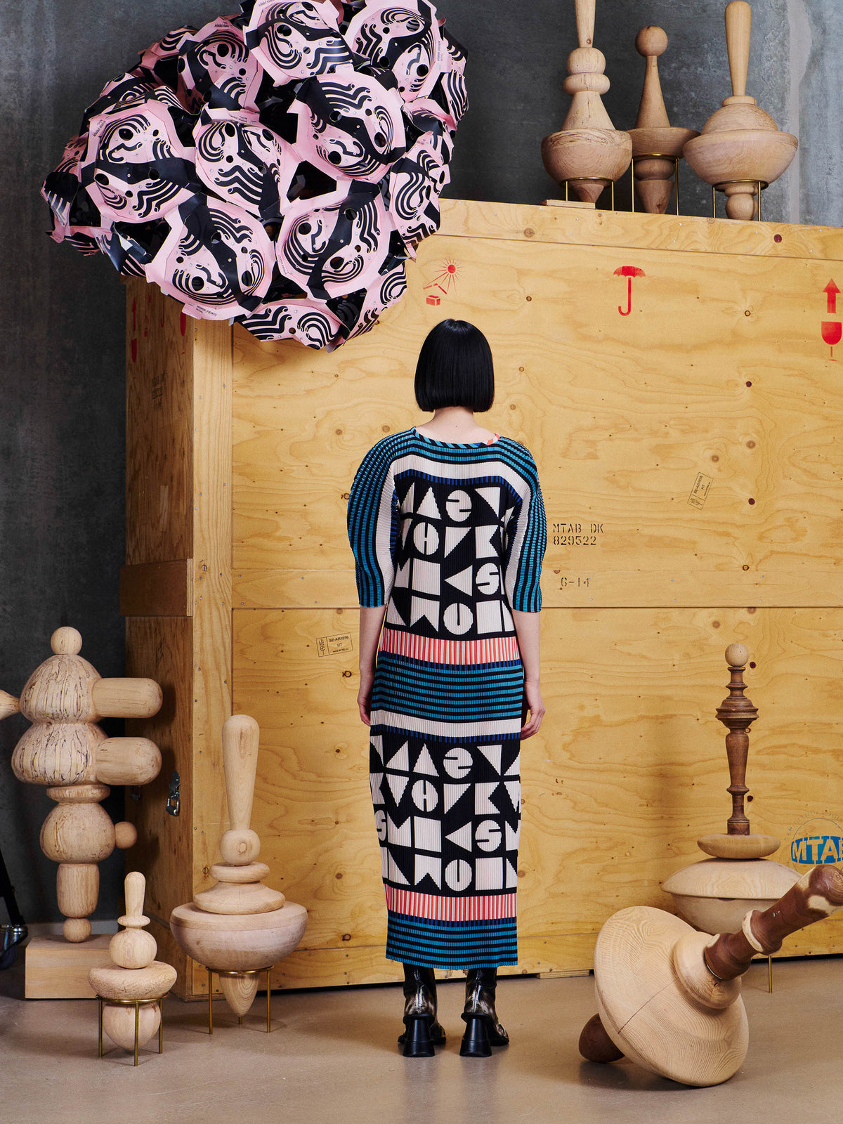Back view of model wearing the Henrik Vibskov Lupu Plisse Dress in Vibs In Bobs, showing the geometric pattern, striped panels and midi length.