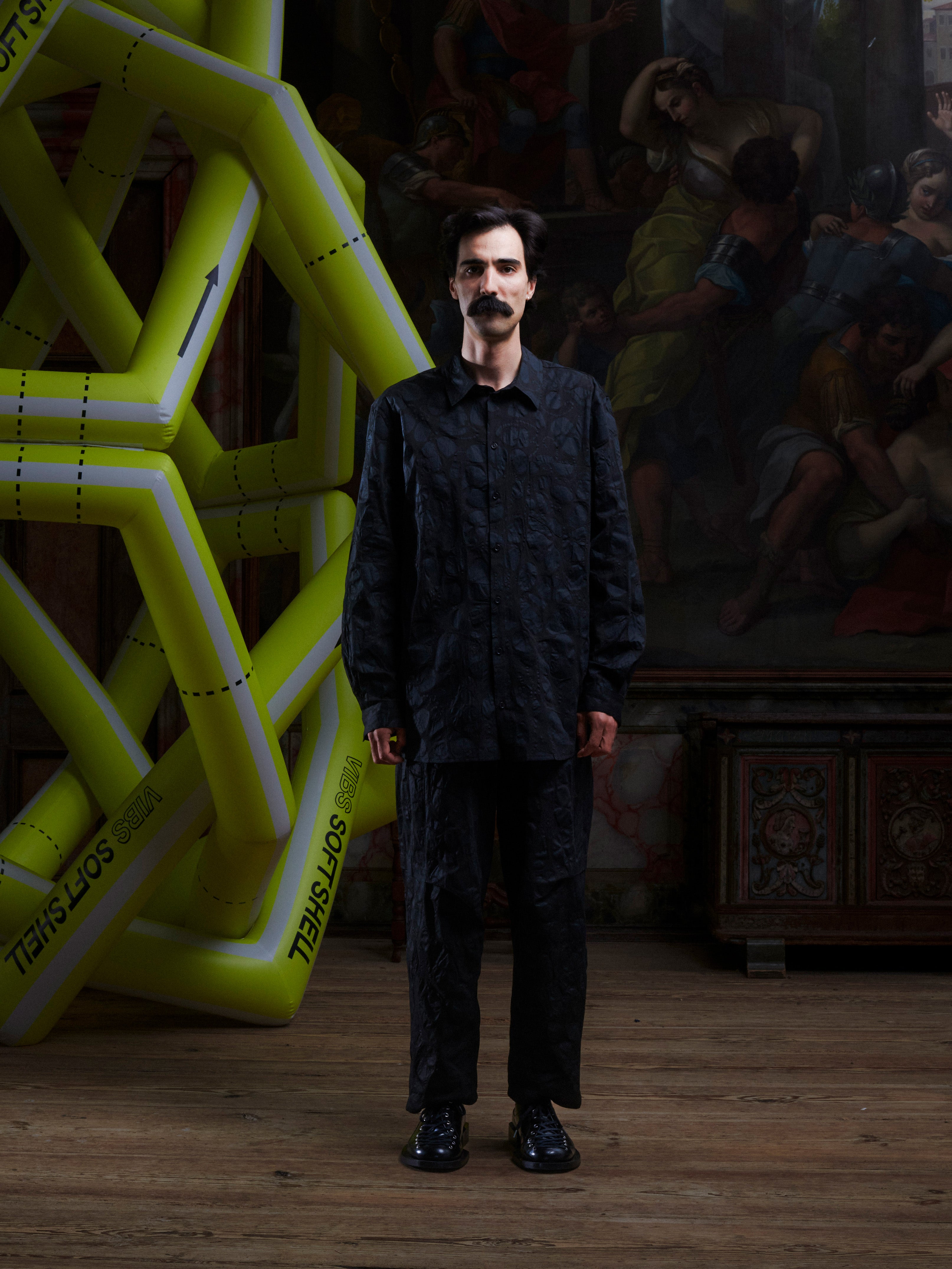 Model wearing the Henrik Vibskov New Blou Shirt in Black Amulets, front view. The model is 181 cm and wears size M, showing the black shirt with tonal amulets pattern, collar, and front chest pocket.