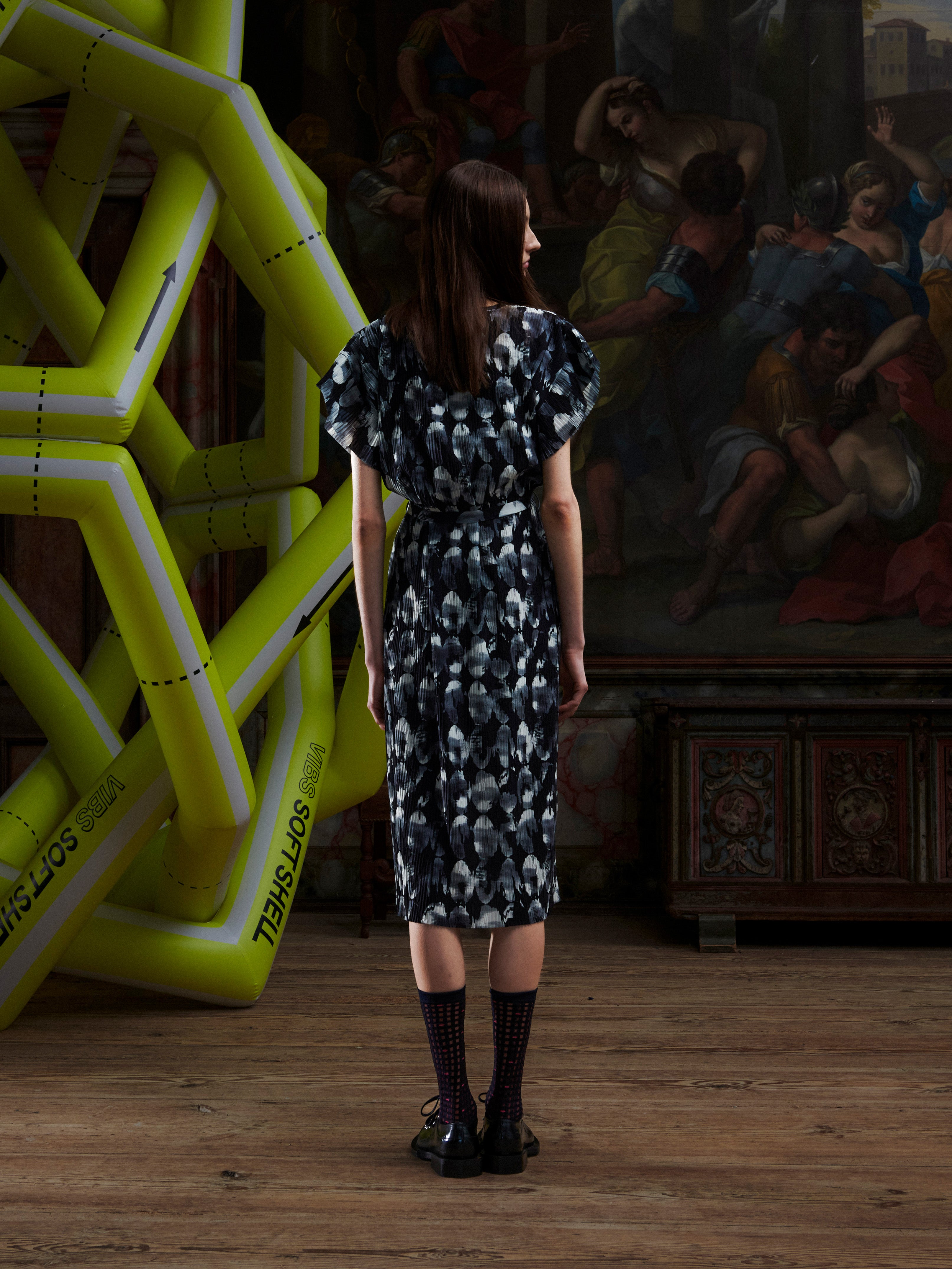 Model wearing the Henrik Vibskov New Pina Plissé Dress in Bursting Eggs, back view, showing the abstract egg illustration across the pleated fabric.