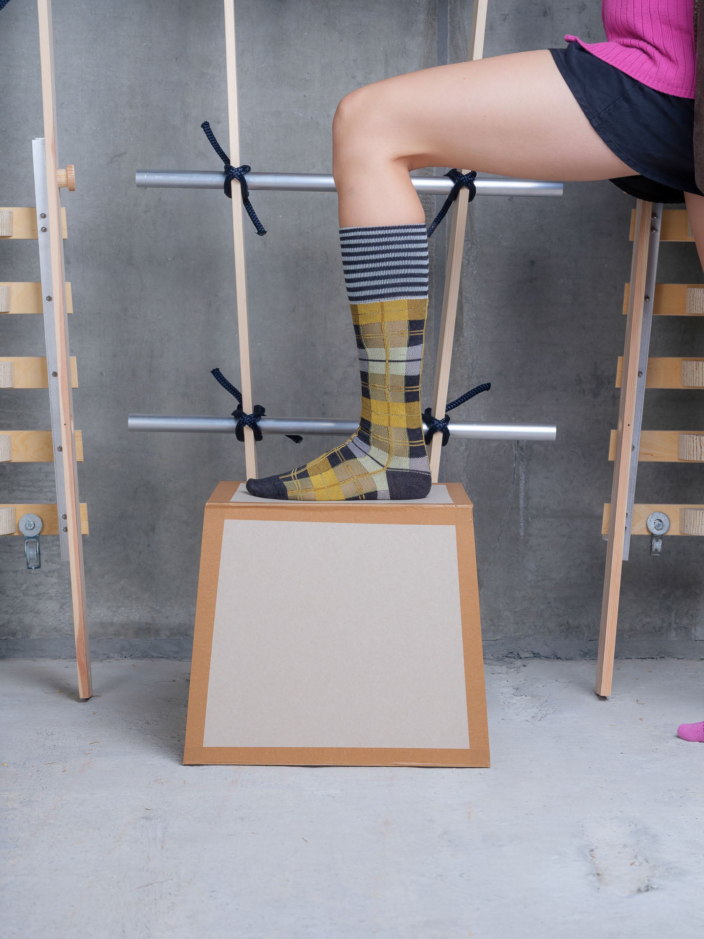 Model wearing Henrik Vibskov Ribbit Knee Sock in grey black dashed checks with mustard yellow panels, striped cuff and contrast toe