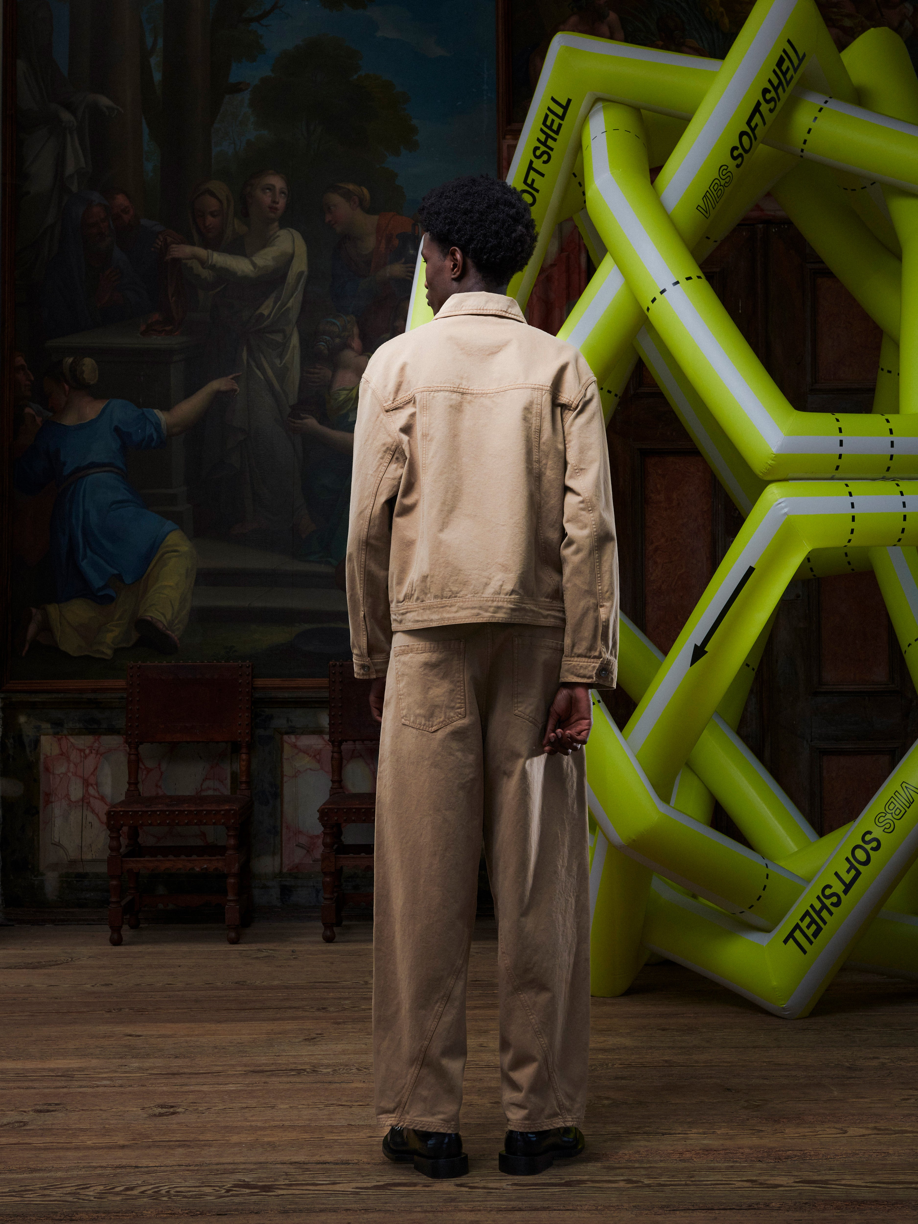 Back view of someone wearing the Dark beige denim jacket from Henrik Vibskov in front of an inflatable structure