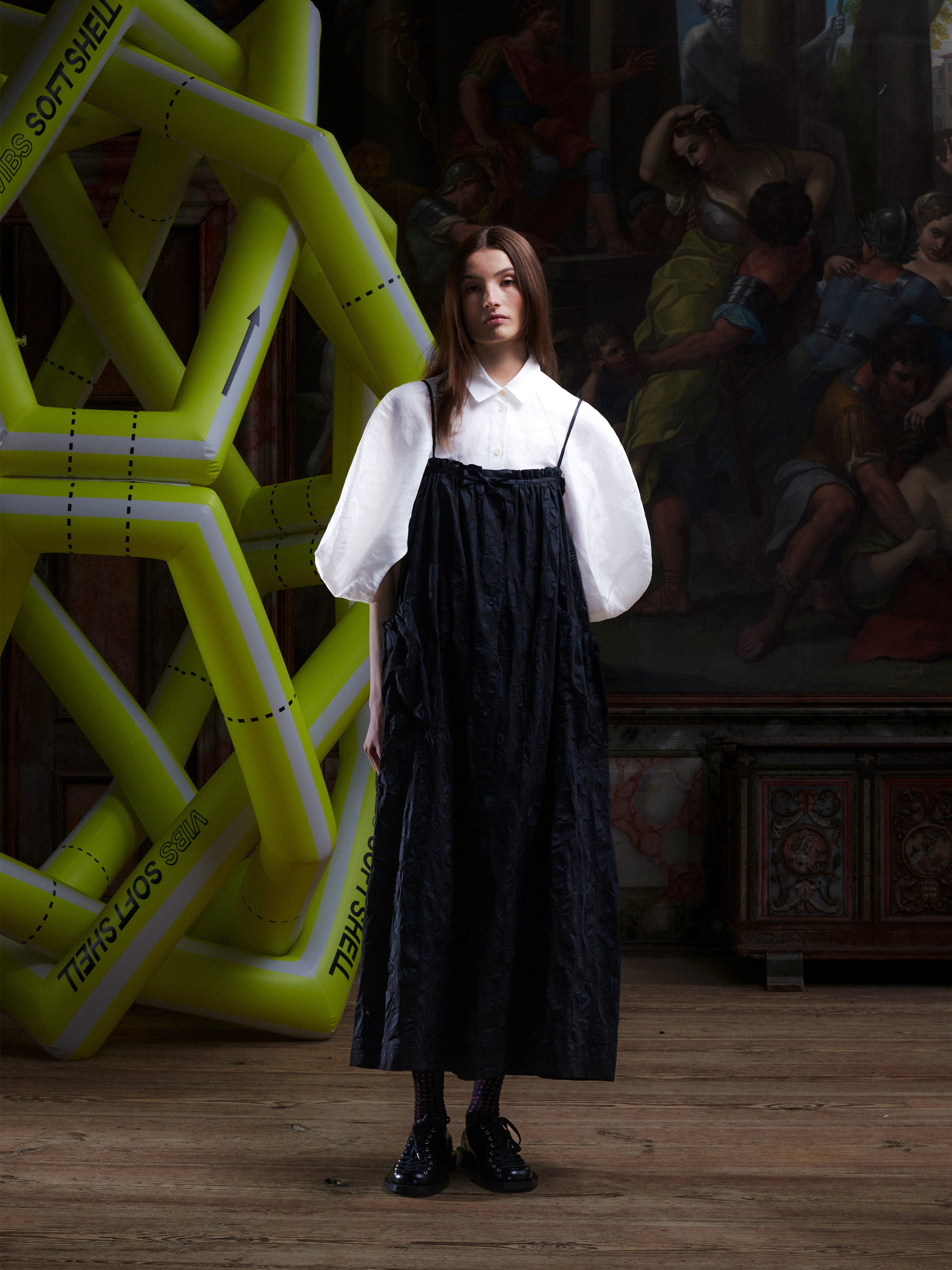 Woman wearing the black-on-black pattern, sleeveless dress on top of a white blouse from Henrik Vibskov.