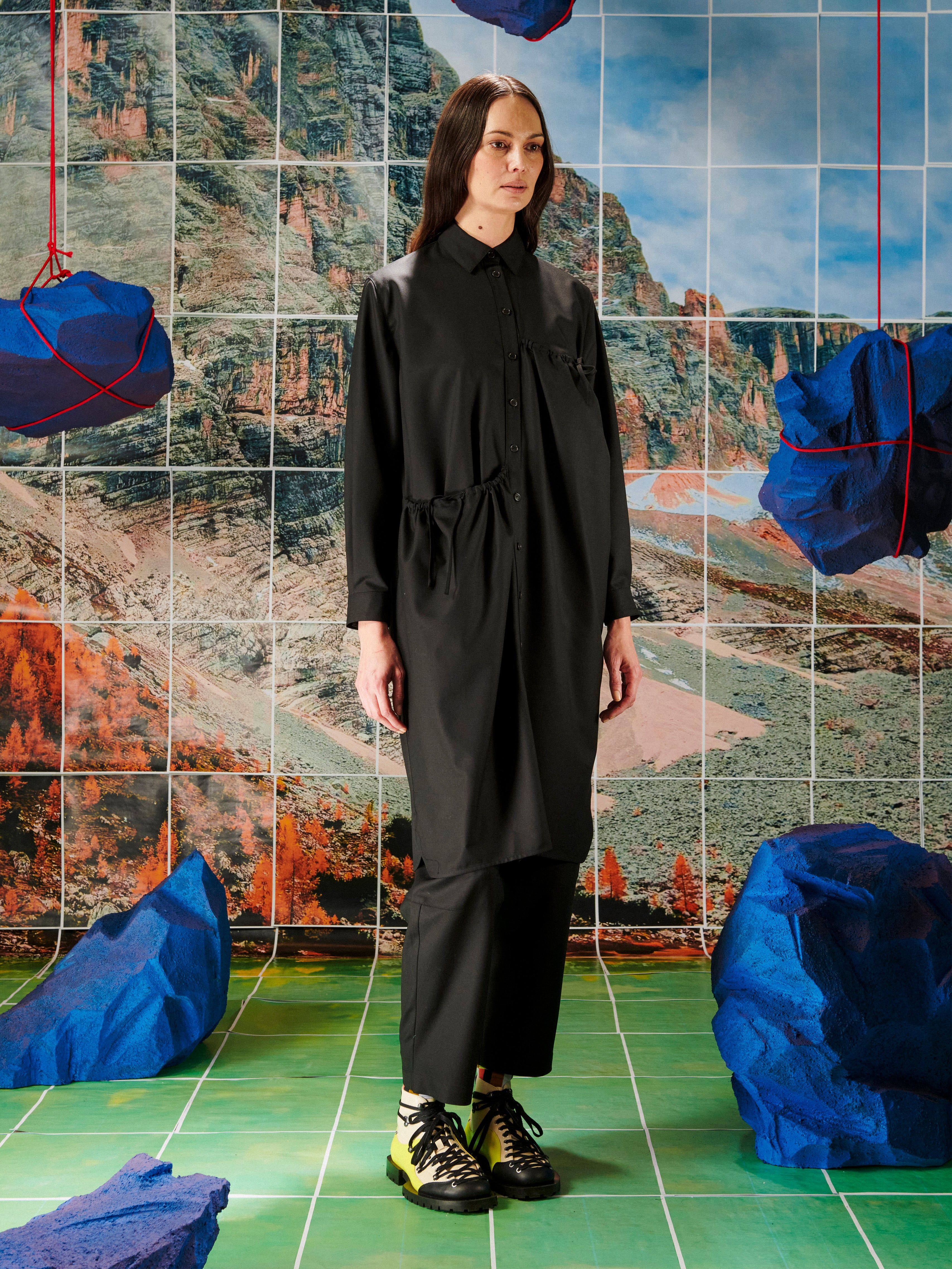 Person wearing a black outfit standing in front of a colorful abstract wall with blue and red sculptures.