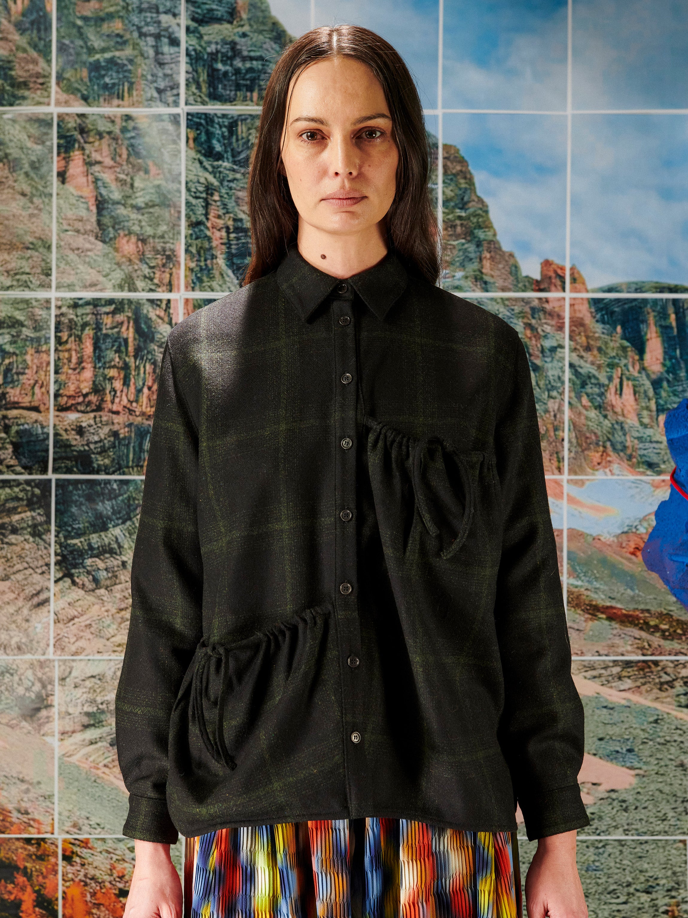 Woman wearing a black plaid shirt in front of a colorful abstract wall.