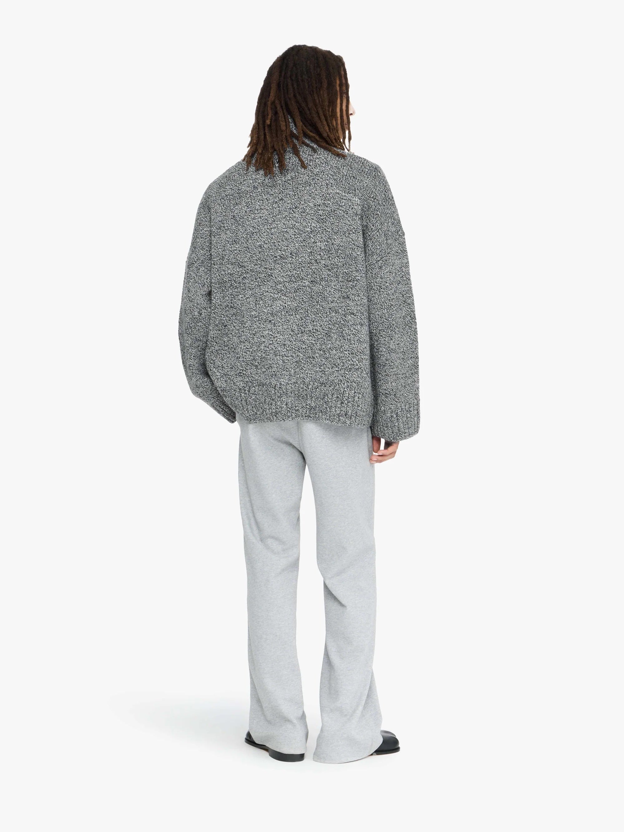 Person wearing a gray textured sweater and light gray pants on a white background