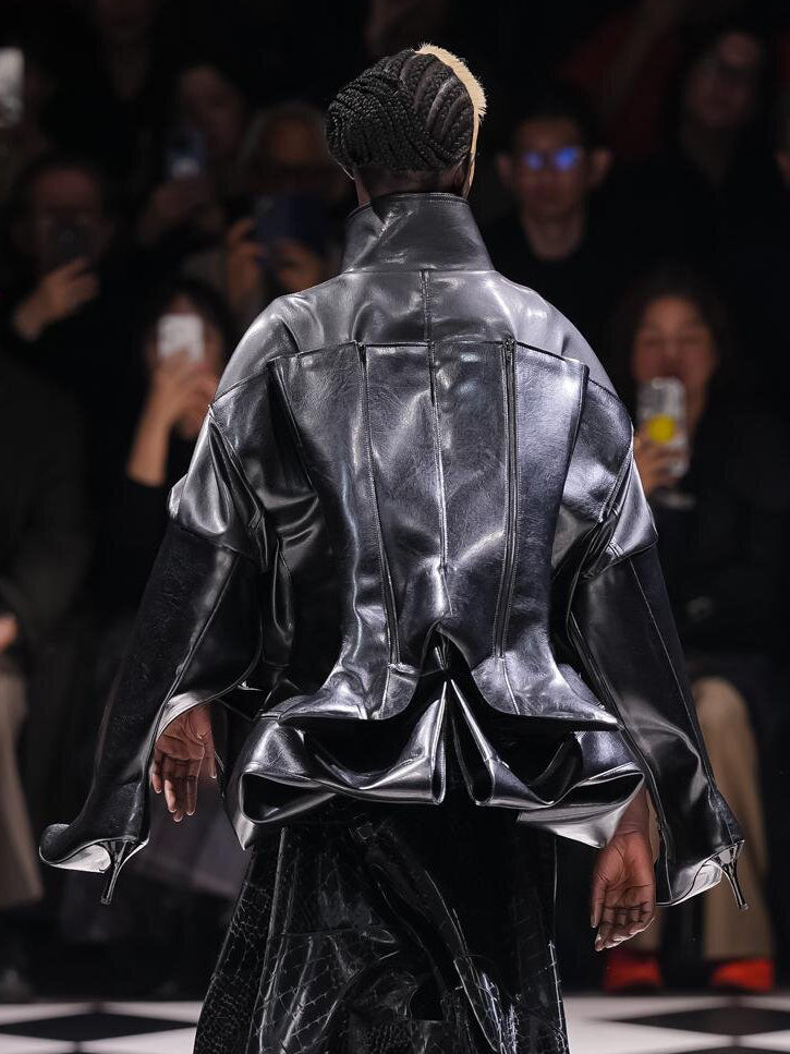 Back runway view of the Junya Watanabe Belted Jacket in Black, showing the panelled construction, extended sleeves and folded sculptural hem.