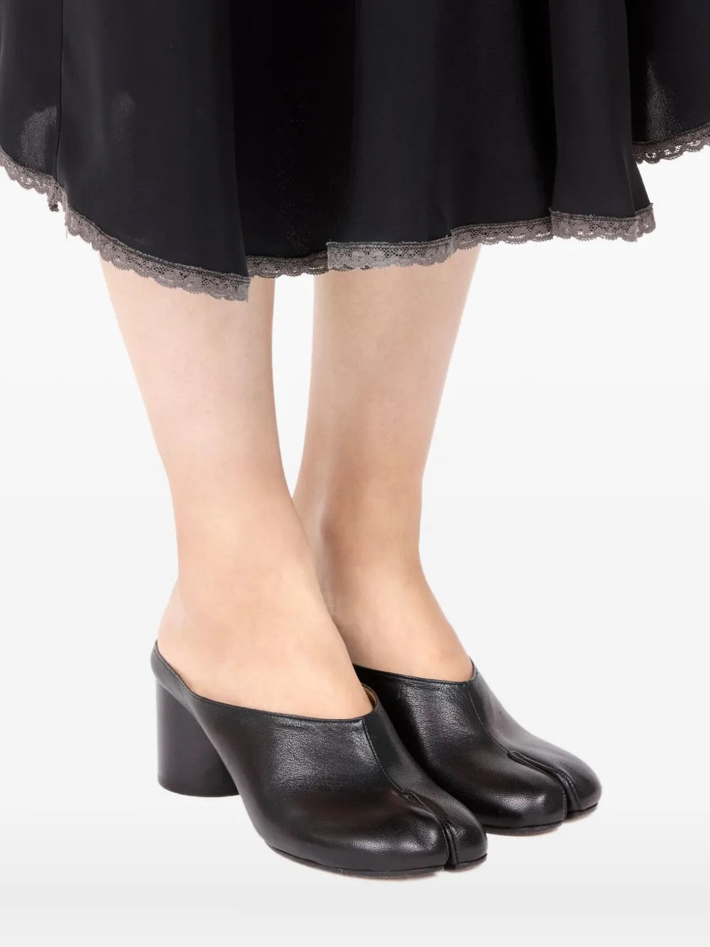 Diagonal front close-up of a model wearing the Maison Margiela Tabi Pump Mules H60 in Black, highlighting the tabi split toe, block heel, and sleek leather finish in a styled look.