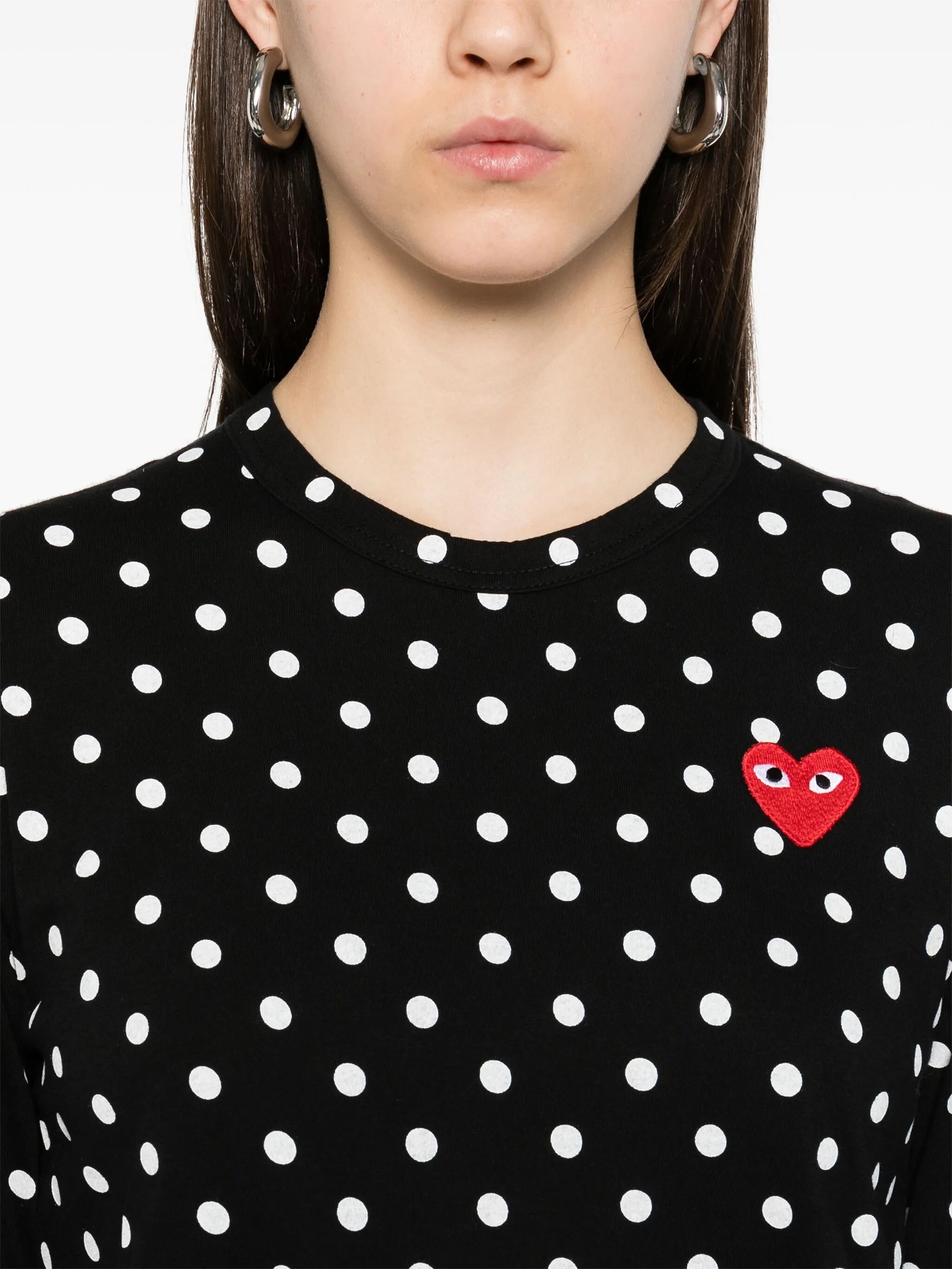 Close-up of Comme des Garçons Play black polka dot shirt showing red embroidered heart logo, round neckline and soft jersey fabric