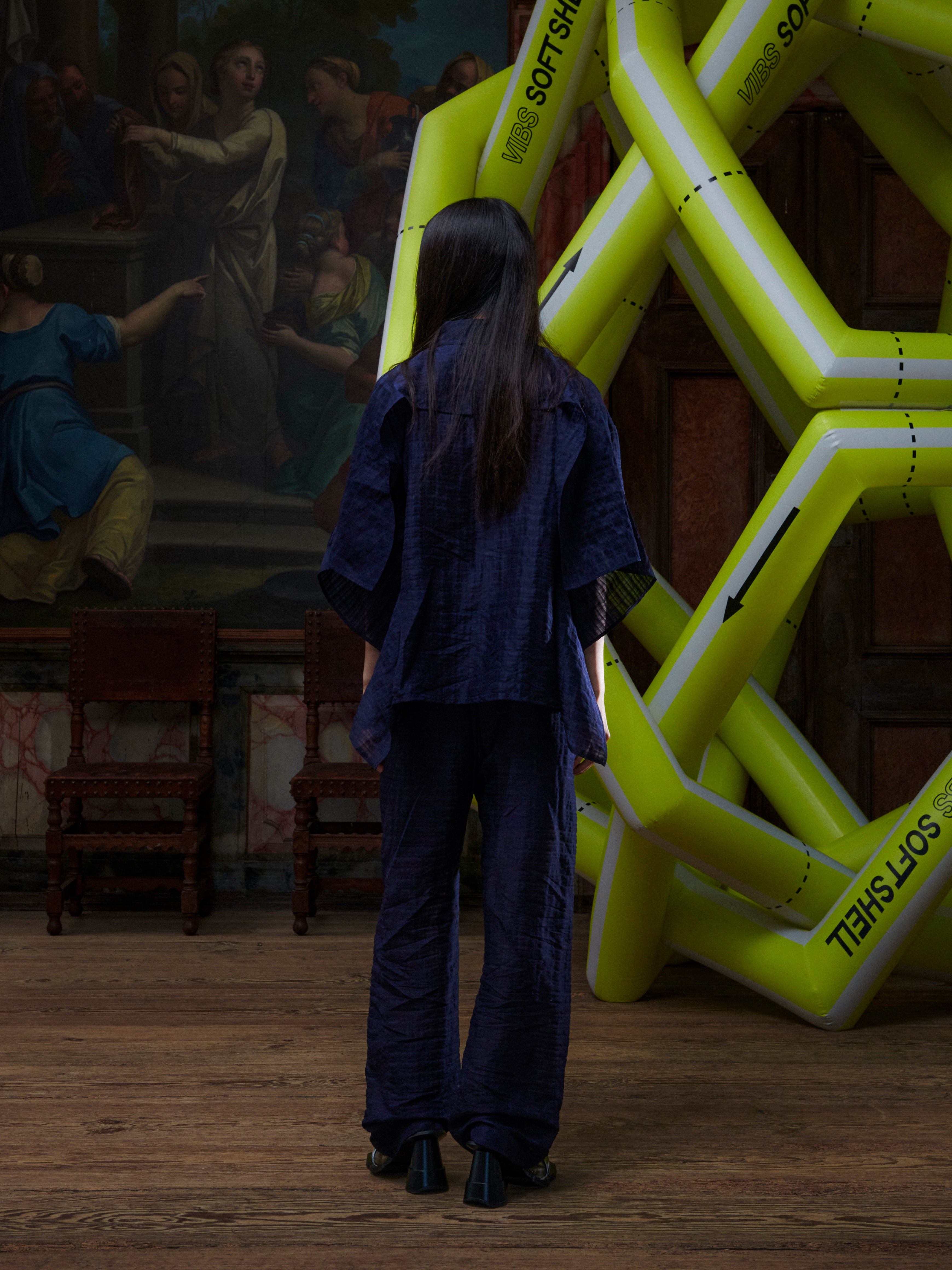 Back view of the female model wearing the Artist Pants in navy from Henrik Vibskov Spring/Summer 2026 Studio Collection, highlighting the straight-leg silhouette and minimalist back design.