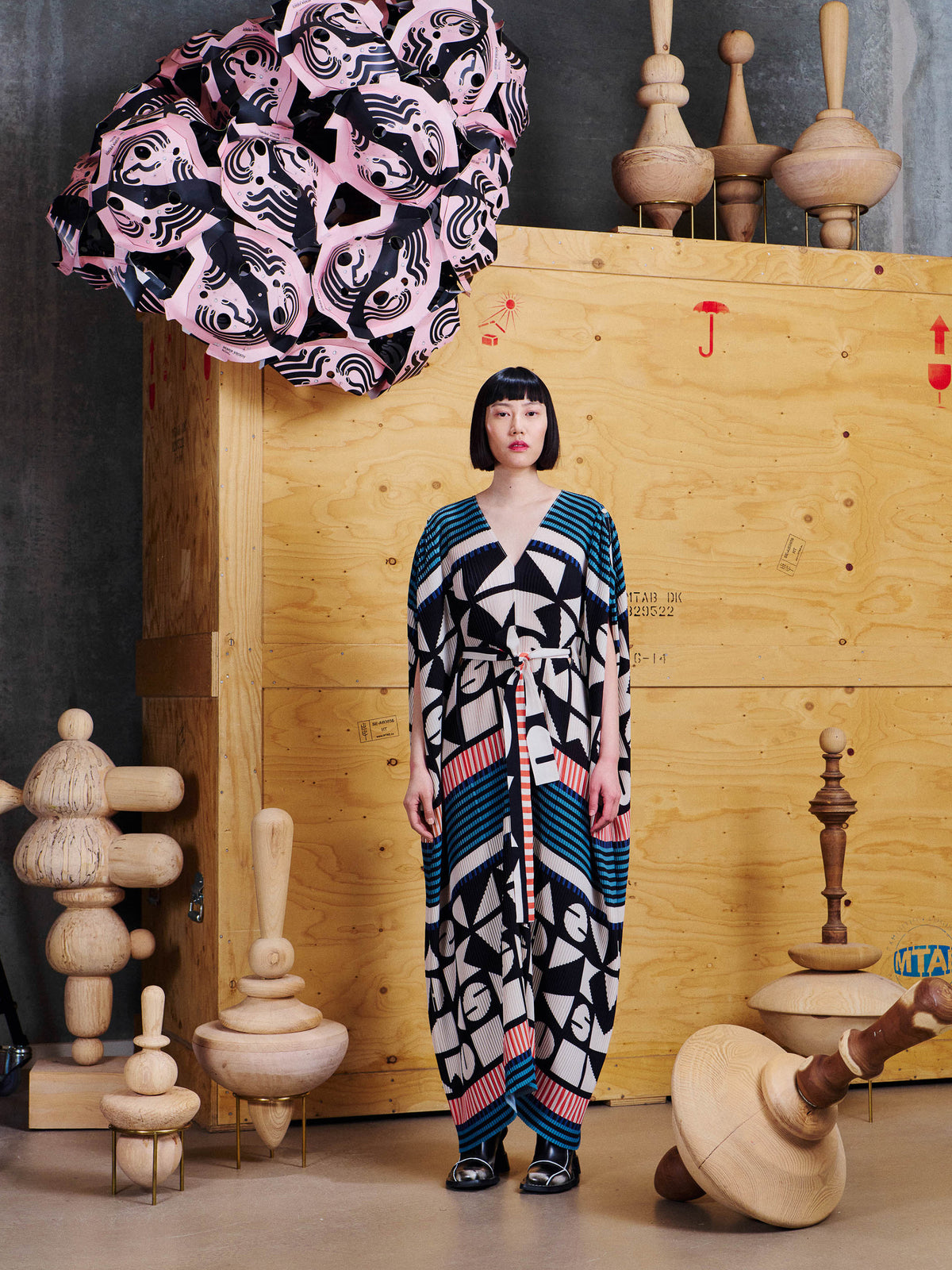 Model wearing Henrik Vibskov Cherry Plisse Kaftan in Vibs In Bobs from the front, showing the V-neck, waist tie and graphic pleated pattern.