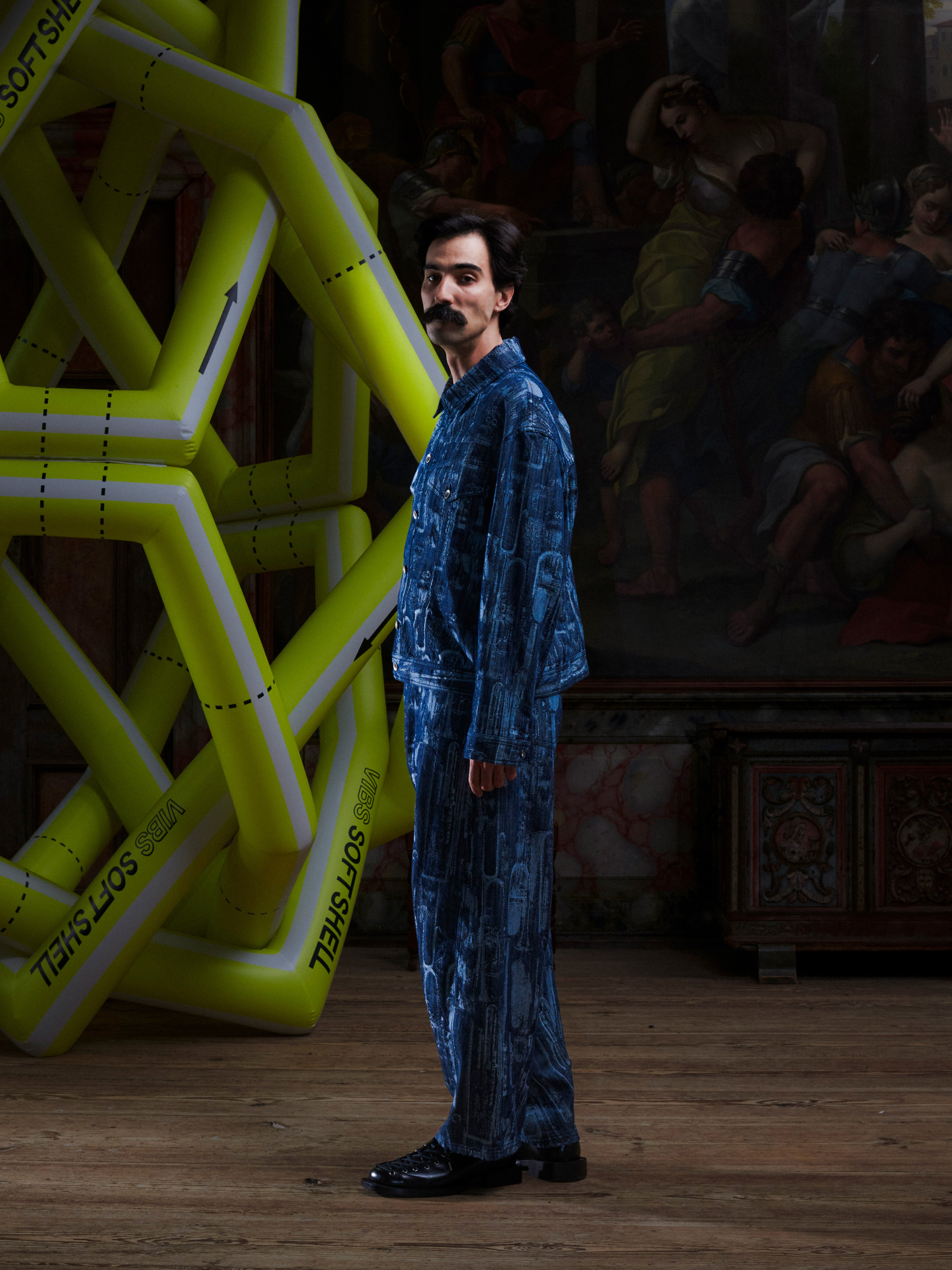 Side view of the male model in the Curved Denim Pants, highlighting the curved leg shape, side pockets, and printed denim. Model is 185cm tall and wears size M.