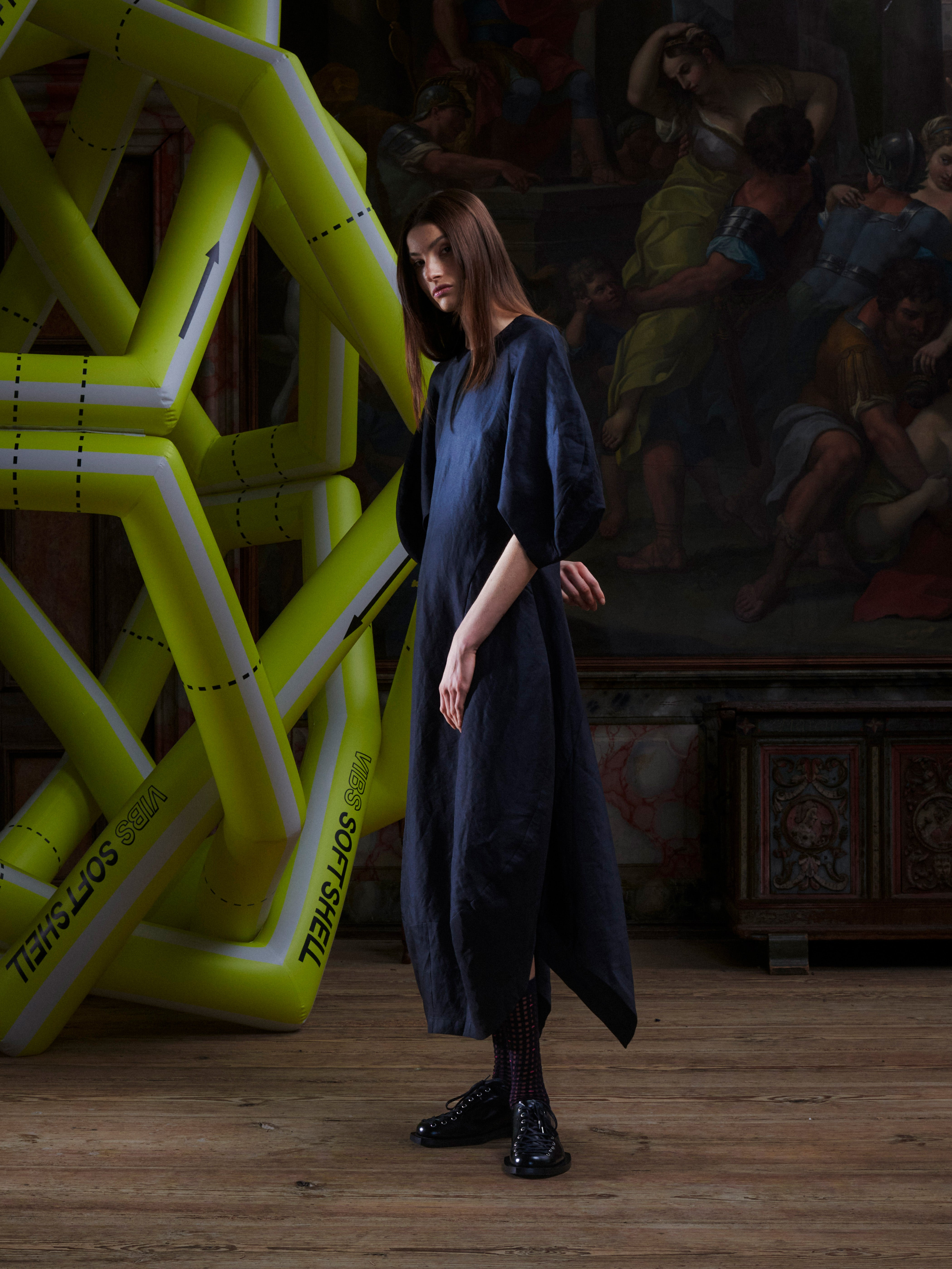 Side view of model wearing the Double Bass Dress in Black, highlighting the curved hourglass silhouette and low–high hemline.