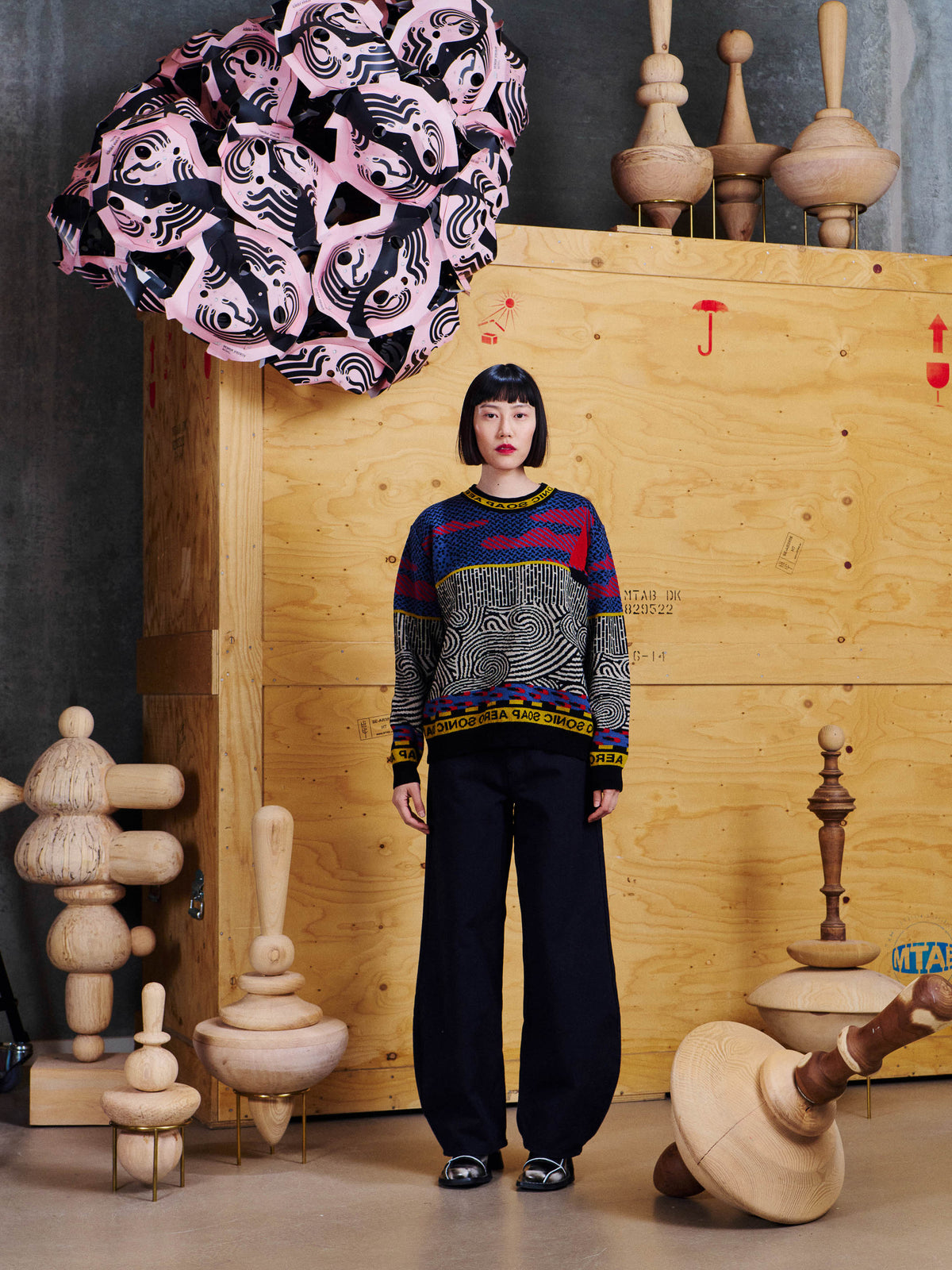 Henrik Vibskov Pipette Pants Anniversary in Black worn front view with a graphic knit sweater, showing the wide curved silhouette and full-length fit.