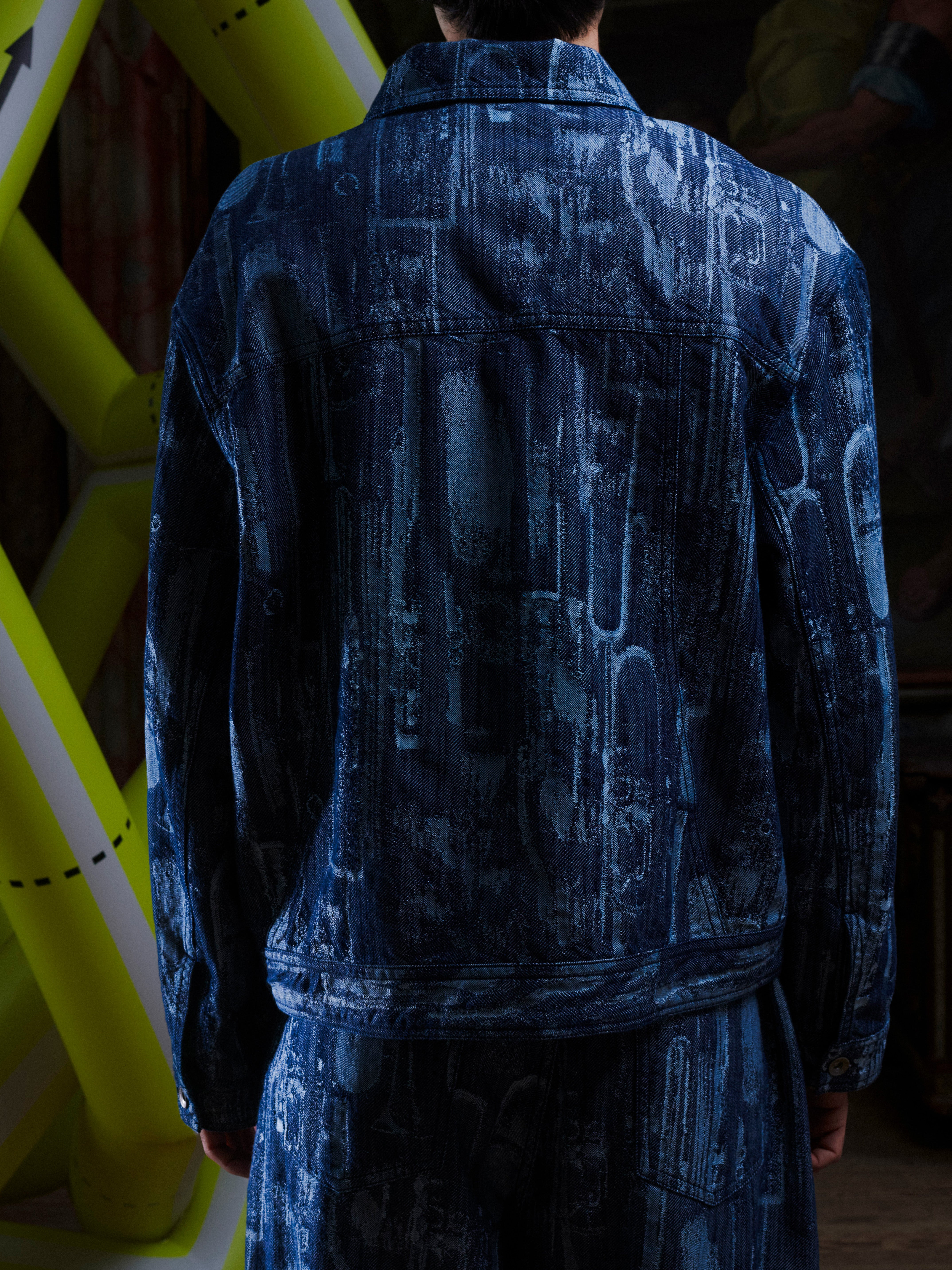 Back view of someone wearing the grey-blue denim jacket with abstract pattern from Henrik Vibskov on a white background