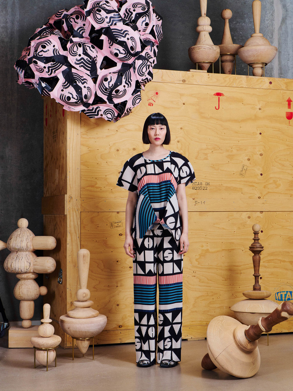 Model wearing Henrik Vibskov Silhouette Plisse Pants in Vibs In Bobs from the front, showing the wide-leg pleated silhouette and bold geometric pattern.