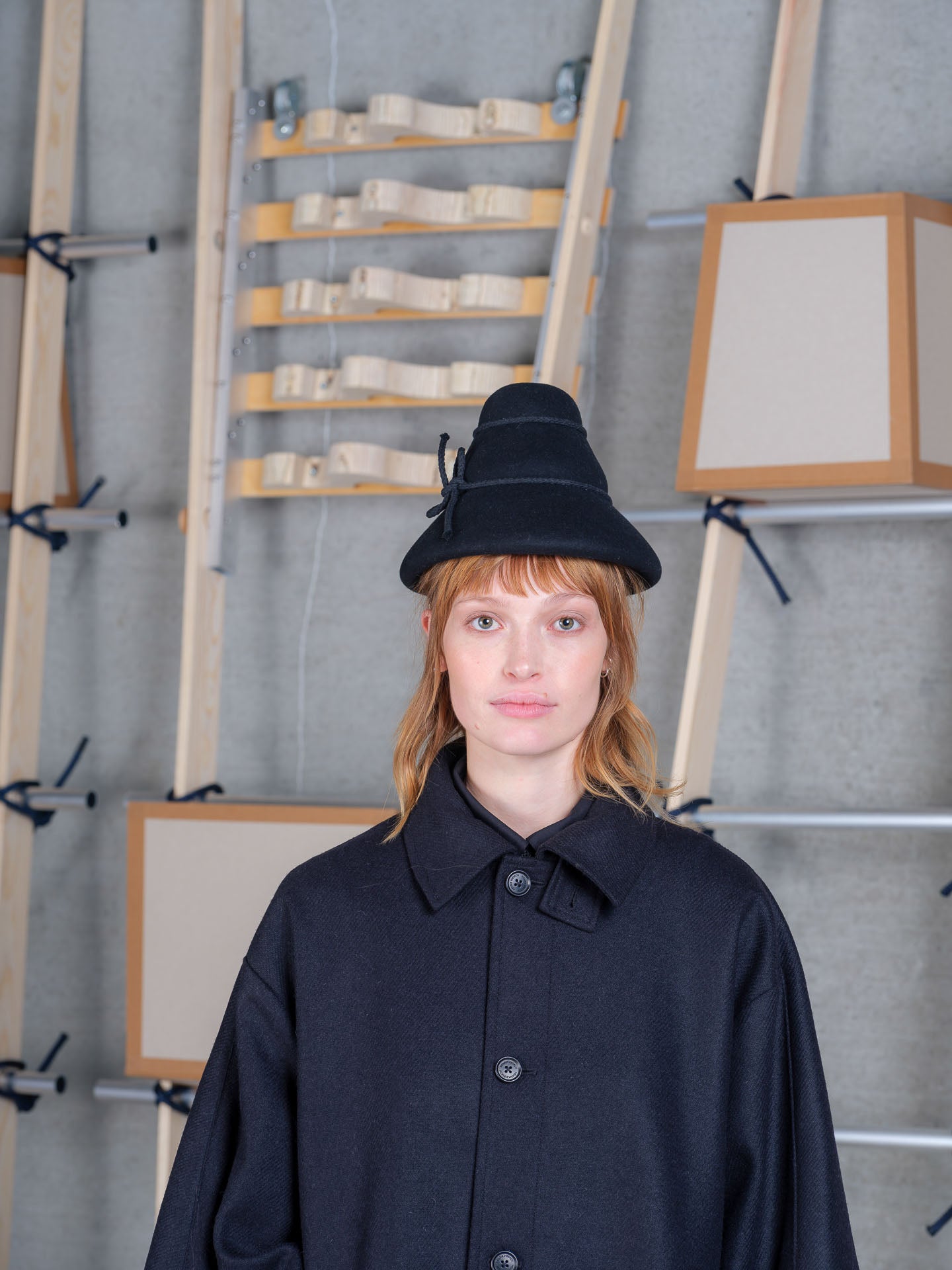 Model wearing the Henrik Vibskov Tower Hat in black with a navy wool coat, front view