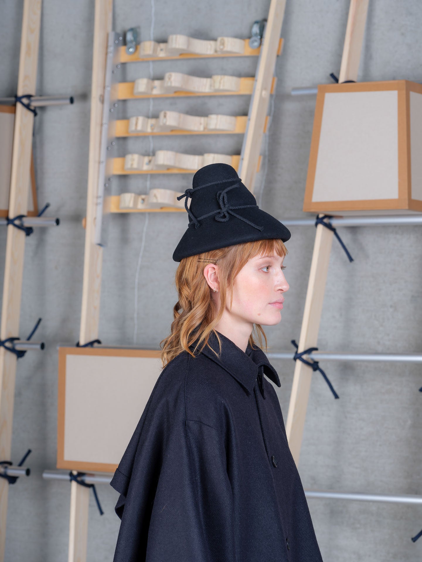 Model in profile wearing the Henrik Vibskov Tower Hat in black, showing the curved brim and rope ties