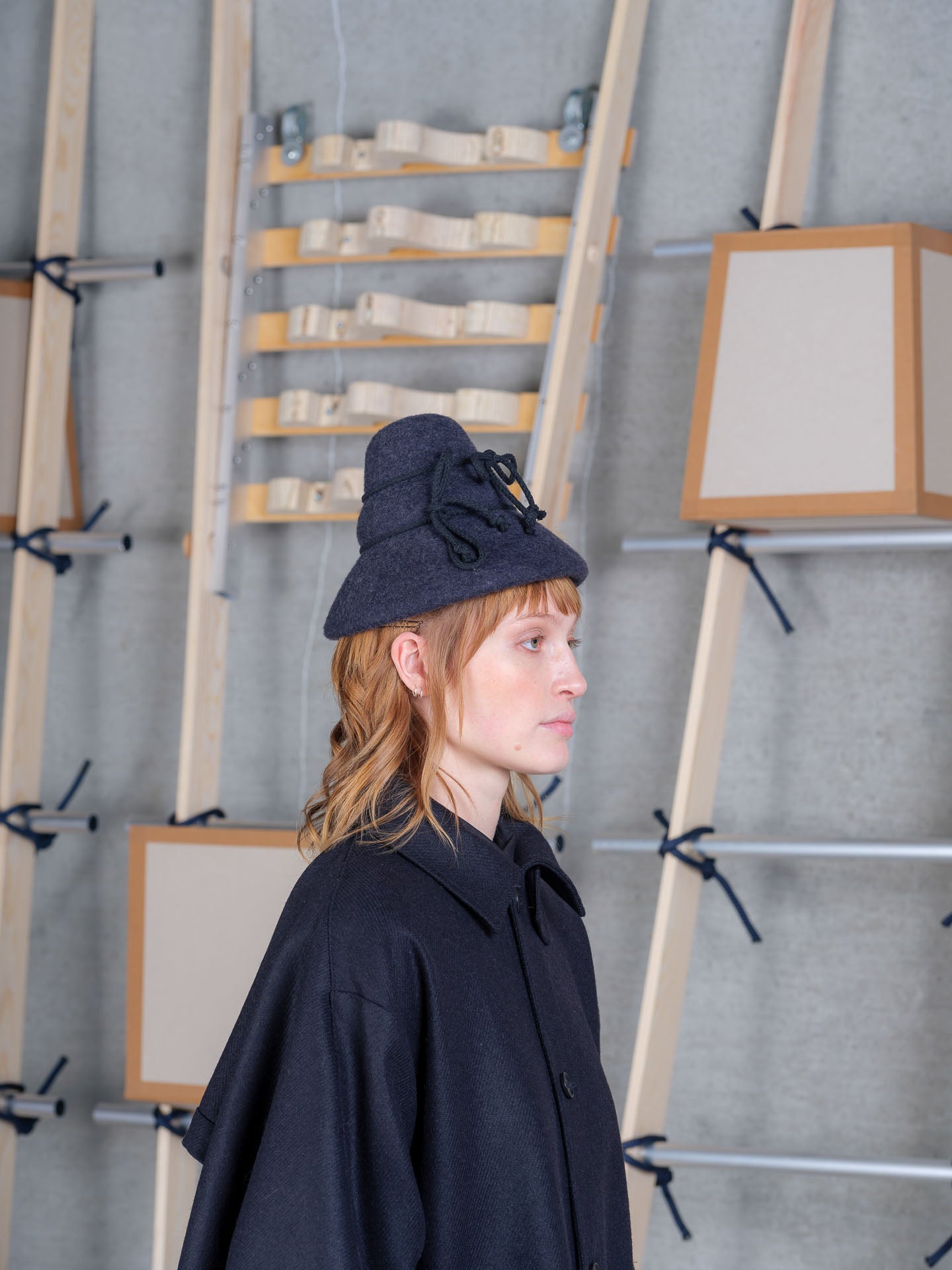 Model in profile wearing the Henrik Vibskov Tower Hat in charcoal, showing the curved brim and rope ties