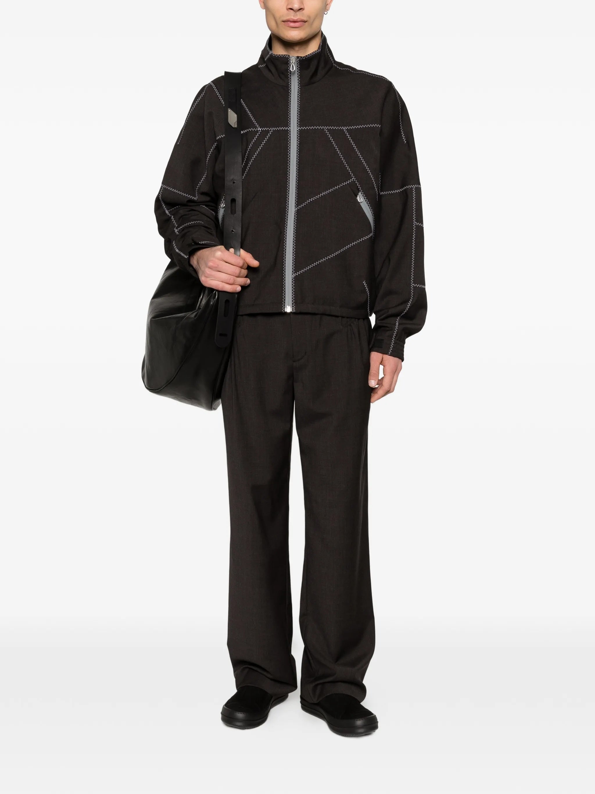 Model wearing the dark brown jacket with white geometric contrast stitching from Kiko Kostadinov on a white background