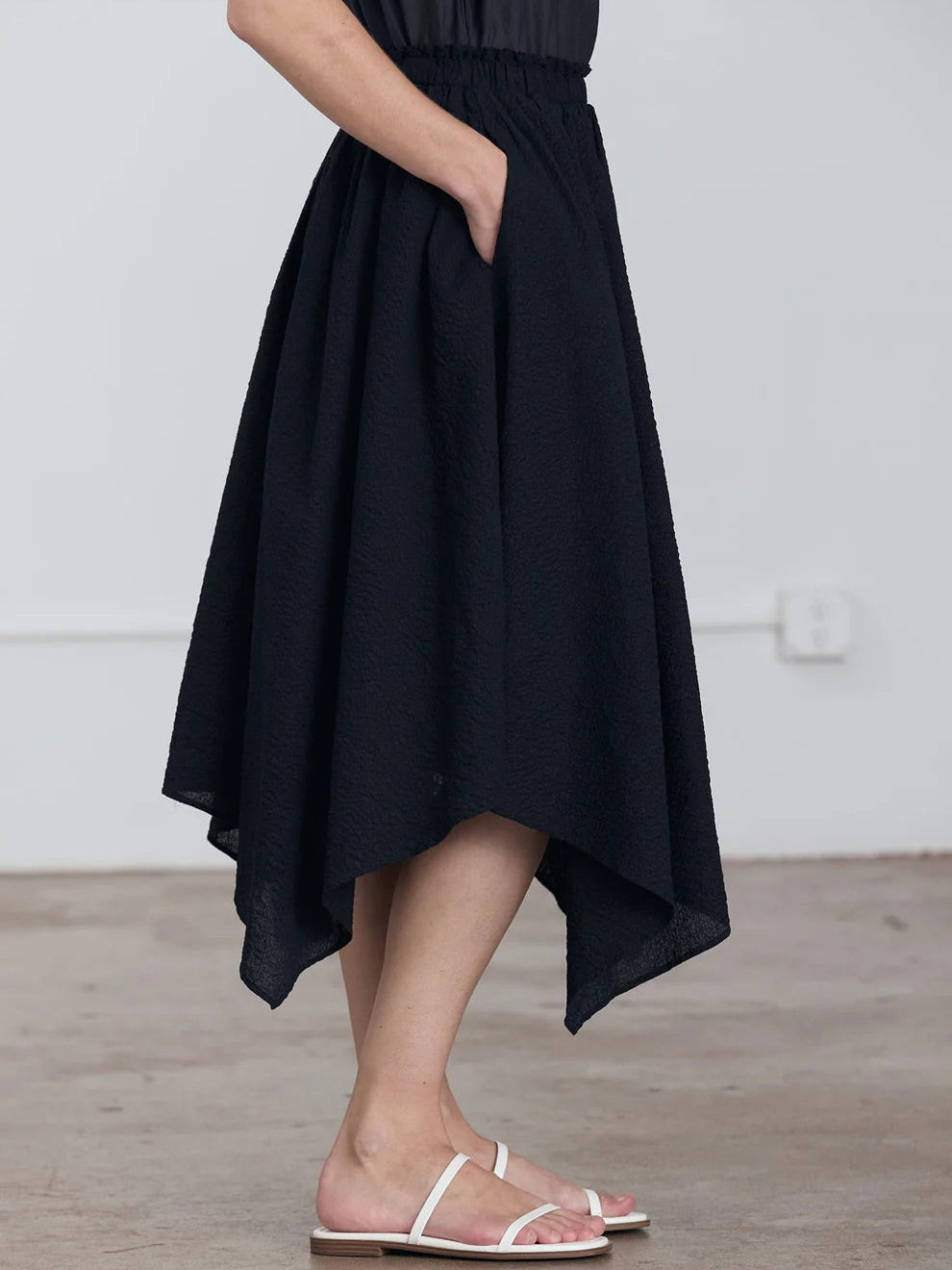 Black Crane Paper Skirt in Midnight - three-quarter front view on model showing asymmetric hem and ripple textured fabric