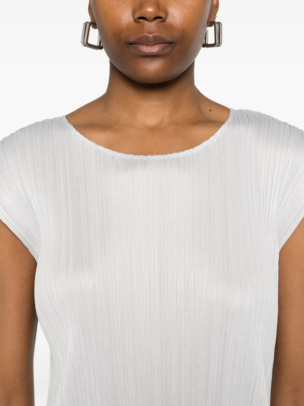 Close-up of the model wearing the light grey, short sleeves, pleated dress from Pleats Please Issey Miyake on a white background