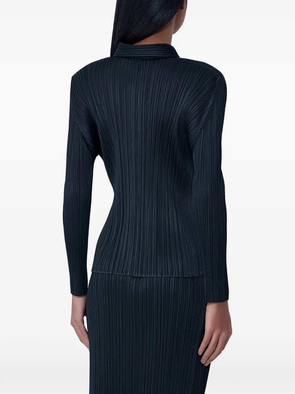 Back view of the model wearing the black, pleated, button-up top with long sleeves from Pleats Please Issey Miyake on a white background