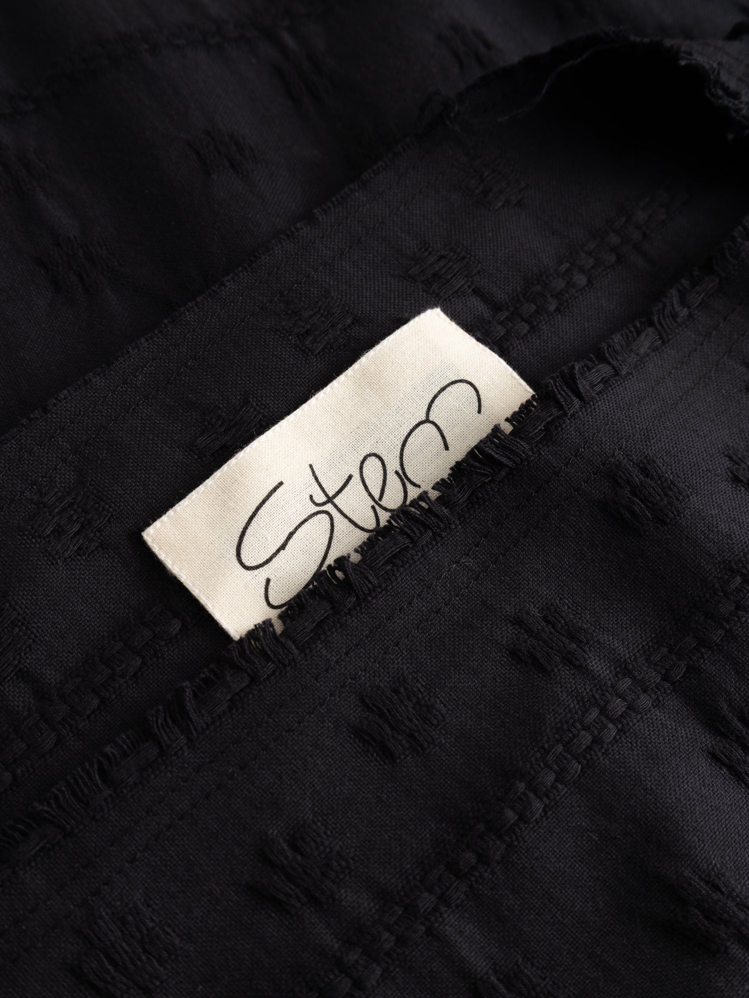 Stem Flower Tee in black, close-up of interior Stem label against woven floral jacquard fabric