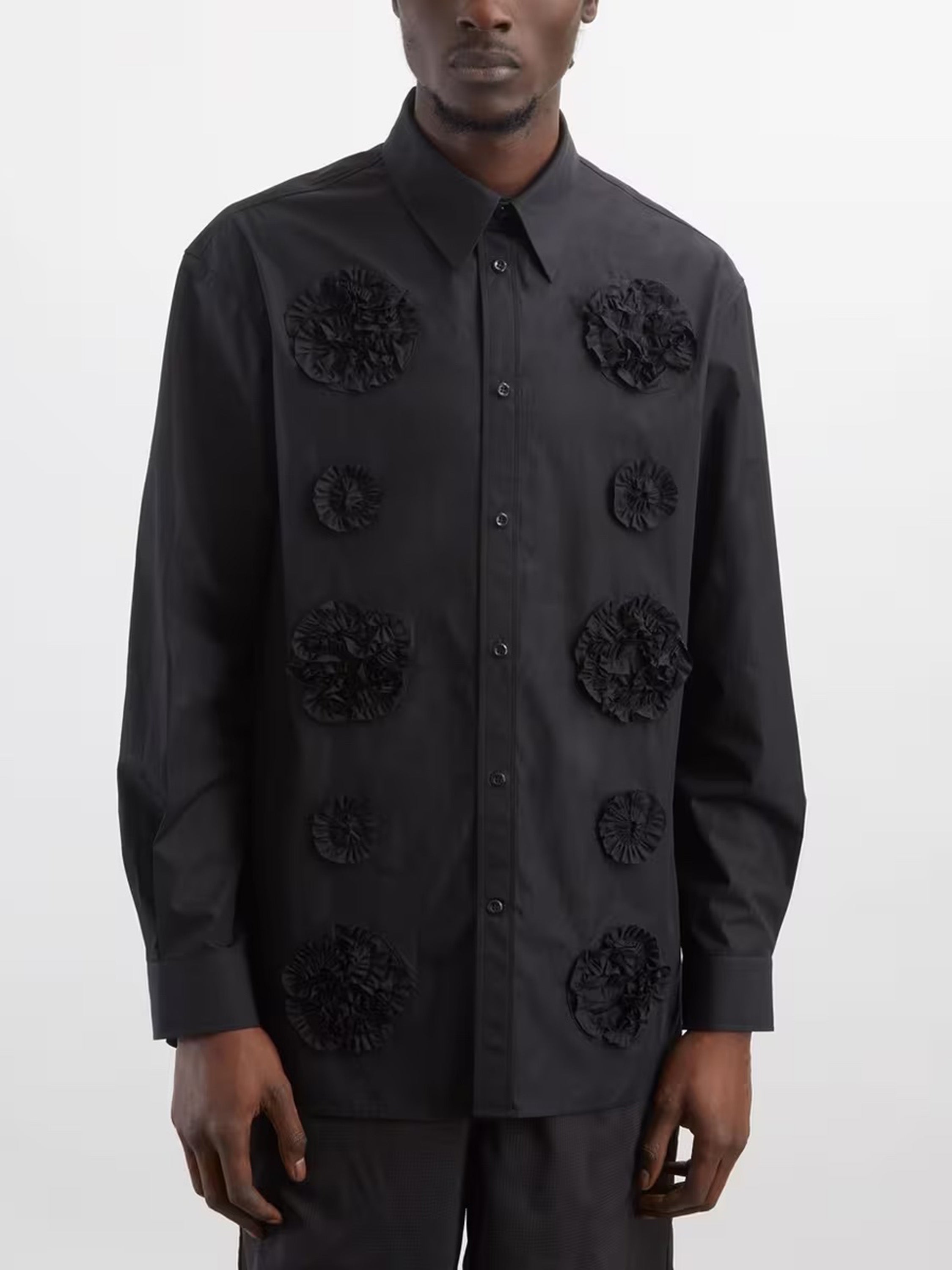 A man wearing the black shirt with flower frill details from Simone Rocha on a grey background
