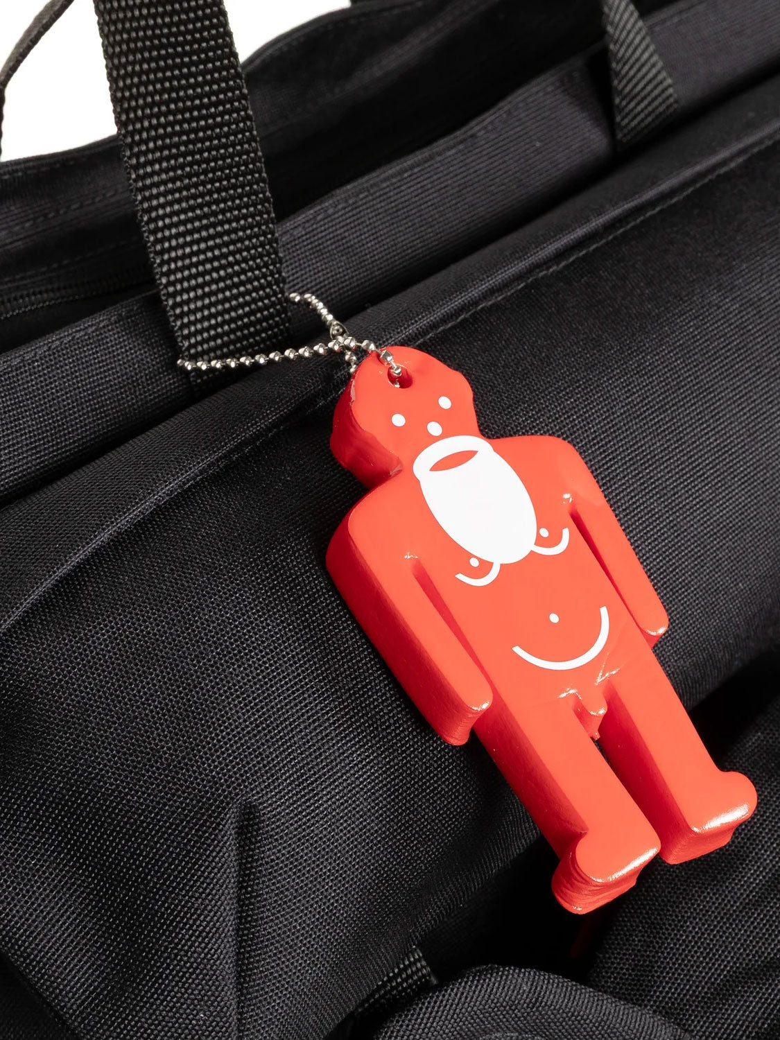 Close-up of red Walterman charm attached to the black Walter Van Beirendonck x Eastpak Walter Carry Bag
