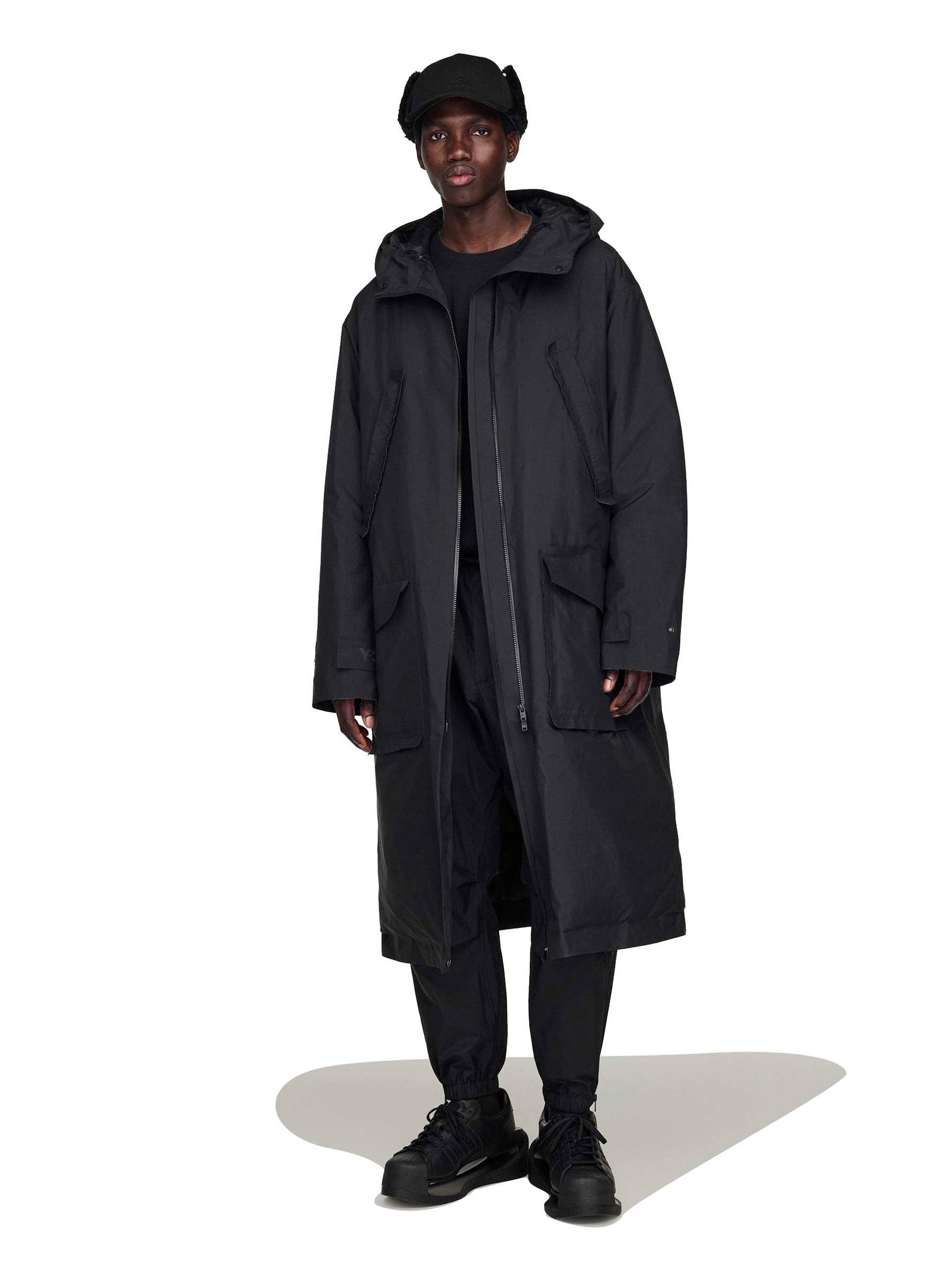 Person wearing an unzipped black coat with hoodie from Y- 3 on a white background