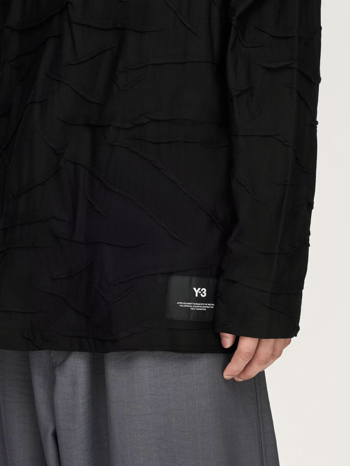 Close-up of the Y-3 Platform Oversized Long Sleeve Tee showing the textured pleated fabric and Y-3 logo patch at the hem.